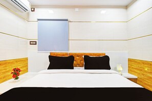A hotel room with a bed, a nightstand, a lamp, and a window with a blind.