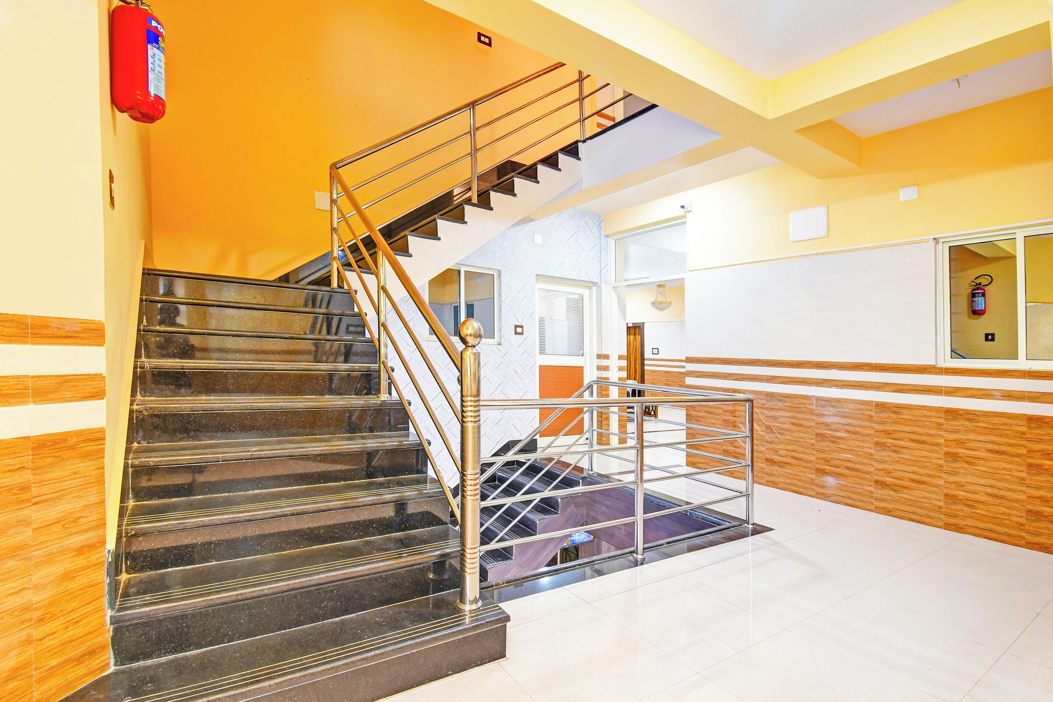 A staircase with metal railings leading to an upper floor, a fire extinguisher mounted on the wall, and a patterned wall design.