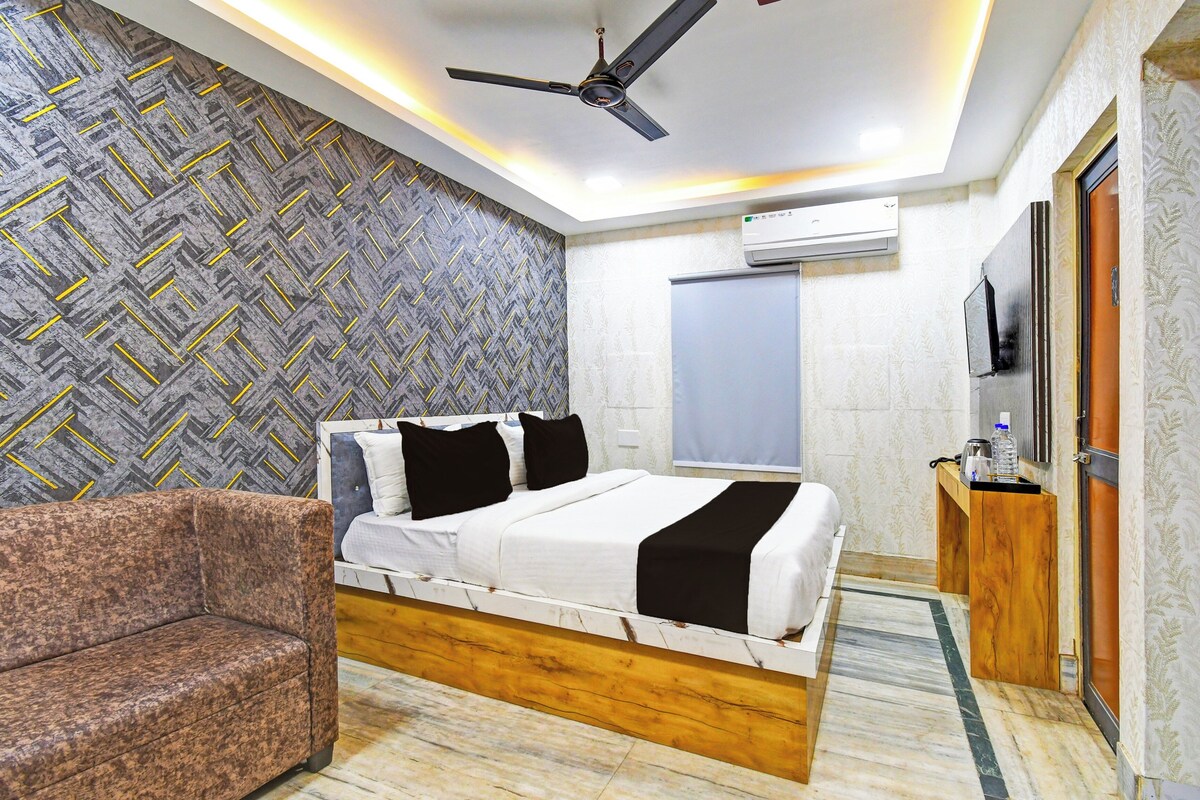 A bedroom with a bed, a chair, a ceiling fan, an air conditioning unit, and a television.