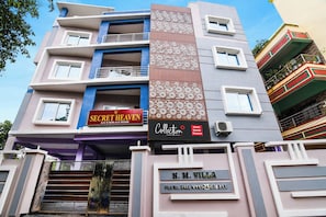 Un hotel de varios pisos con balcones, un letrero que dice 'Secret Heaven A/C & Non-A/C Room' y un letrero que indica 'Collection'.