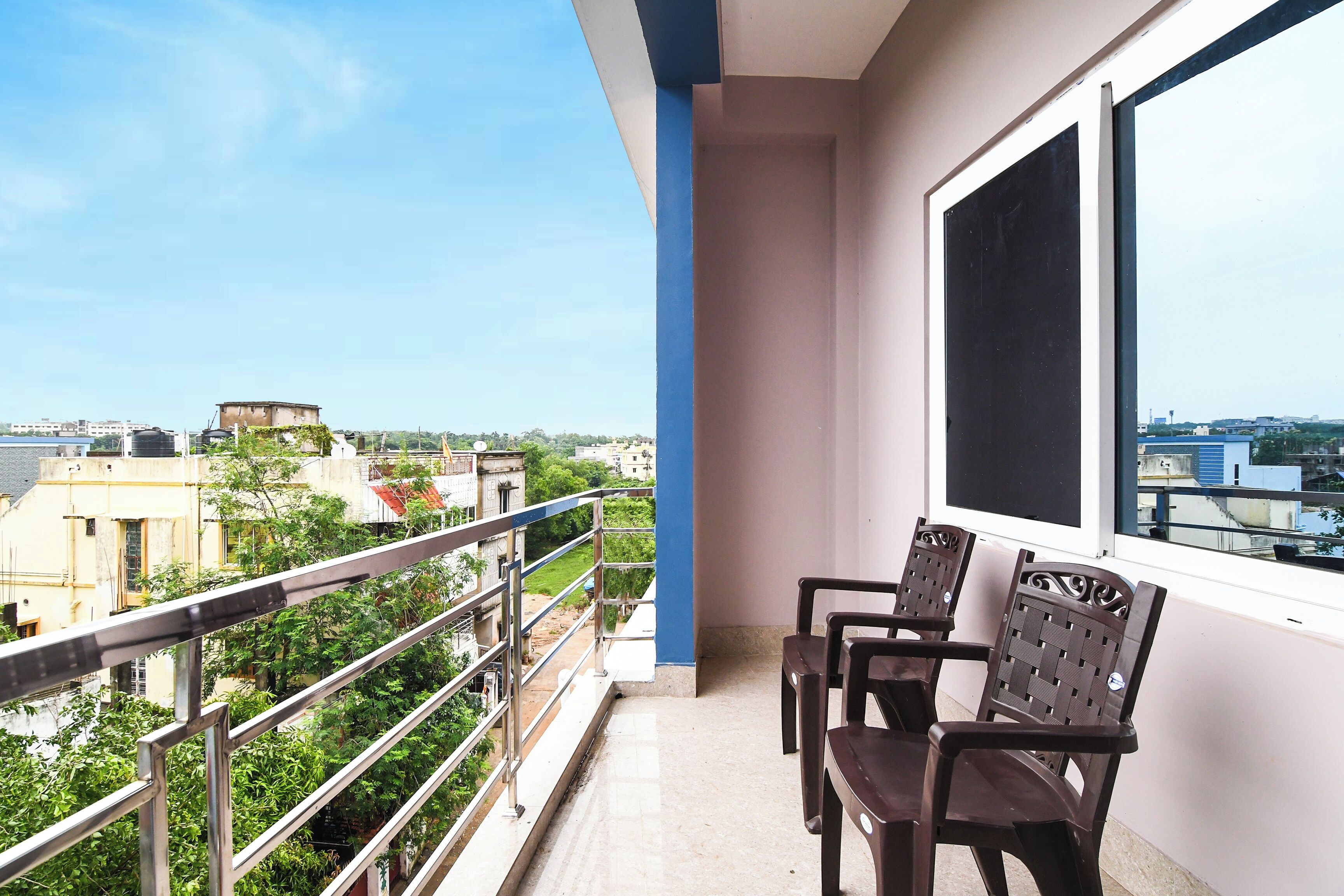 A balcony with a view of a cityscape, a window, and two chairs.