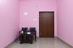 Una habitación con paredes rosas, una puerta de madera, una mesa con sillas y una mesita con una tetera y tazas.