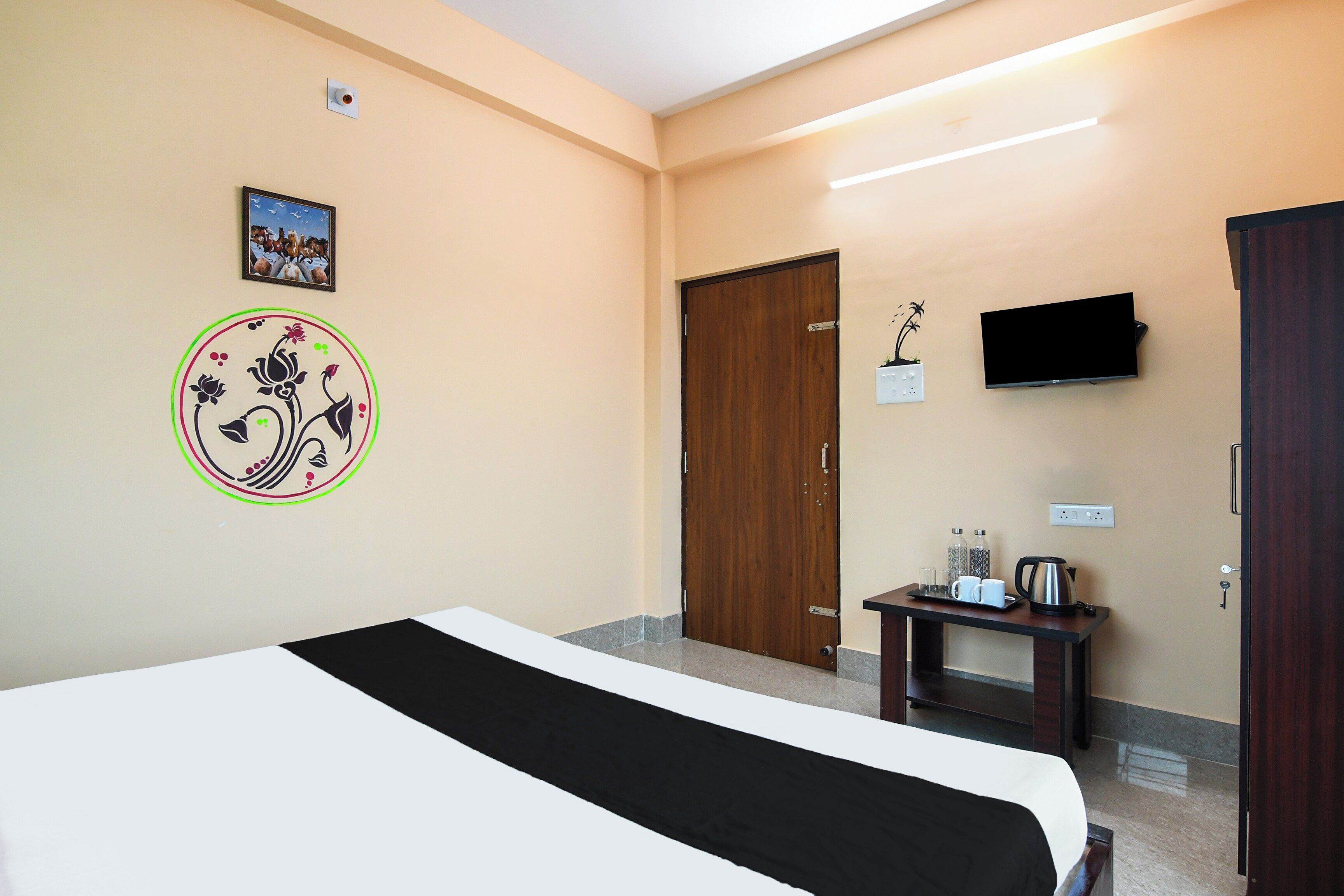 A hotel room with a bed, a television, a door, and a small table with a kettle and cups.