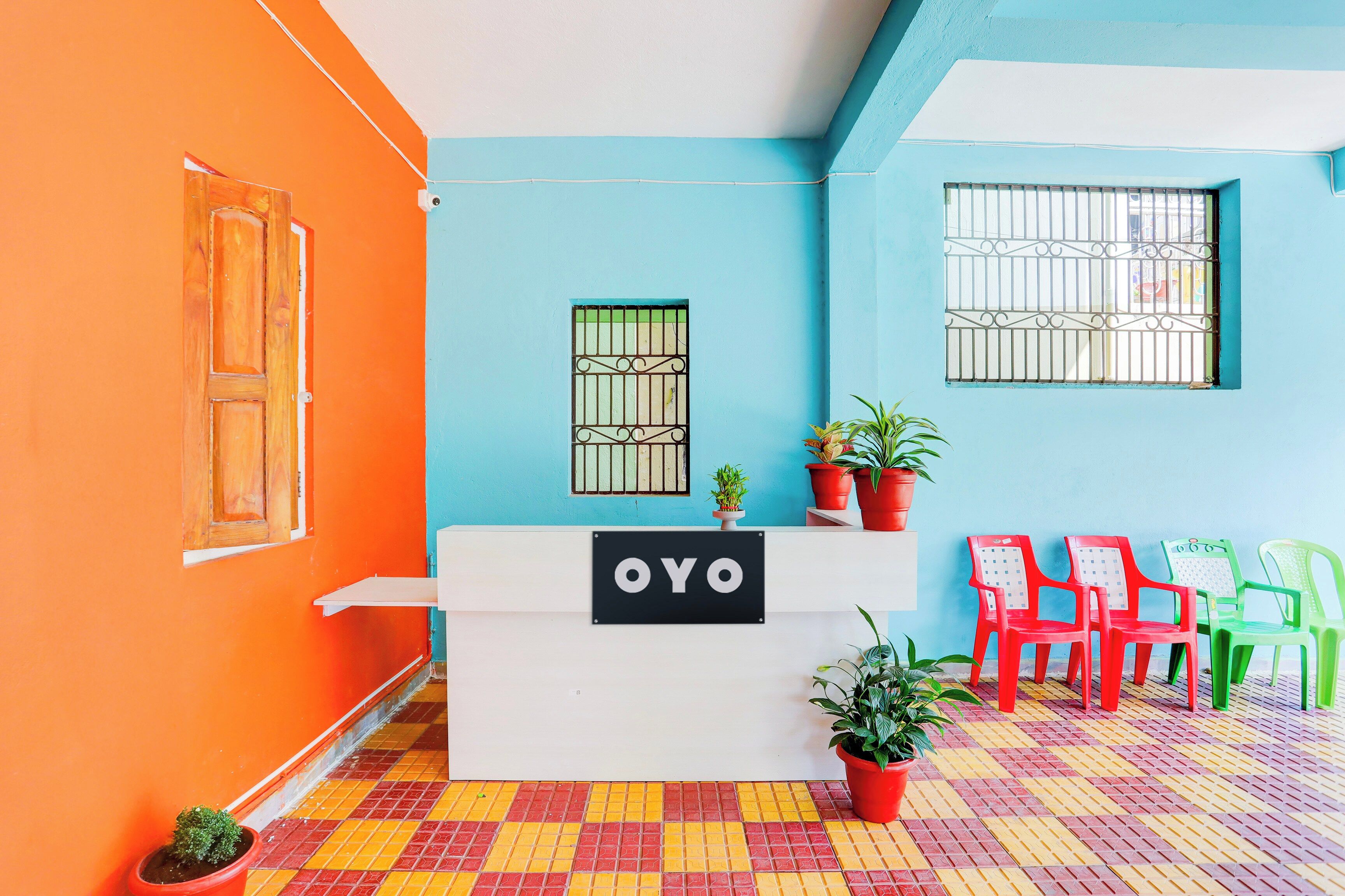 A reception desk with a sign reading 'OYO' in a brightly colored room with orange and blue walls, a tiled floor, and several potted plants.