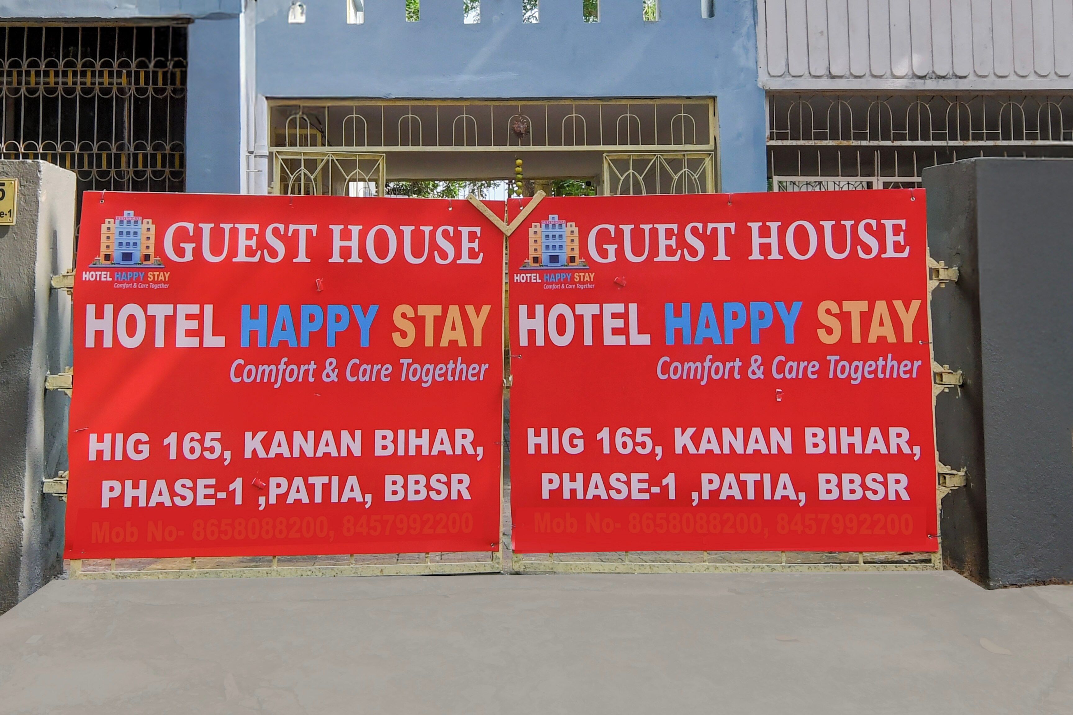 Dos letreros rojos de Hotel Happy Stay, que indican ubicación en Hig 165, Kanan Bihar, Fase 1, Patia, BBSR.