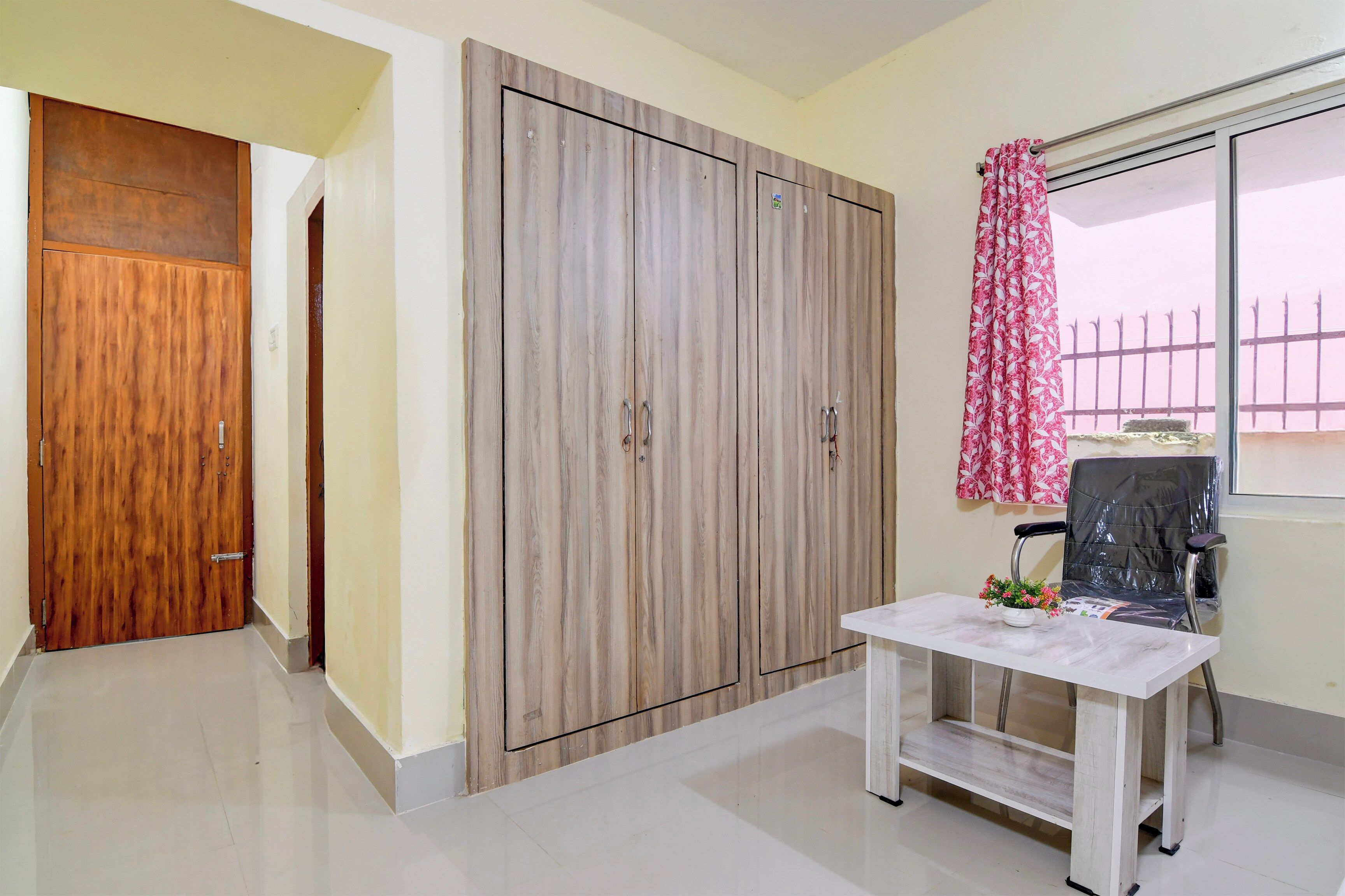 A room with a wooden wardrobe, a table with a vase, and a chair.