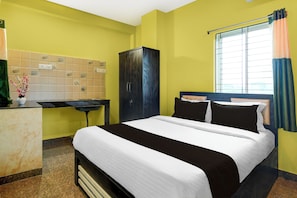 A hotel room with a bed, a wardrobe, a desk with a vase of flowers, and a window with curtains. - Hotel O Royal Avisi Residency (Bhubaneswar)
