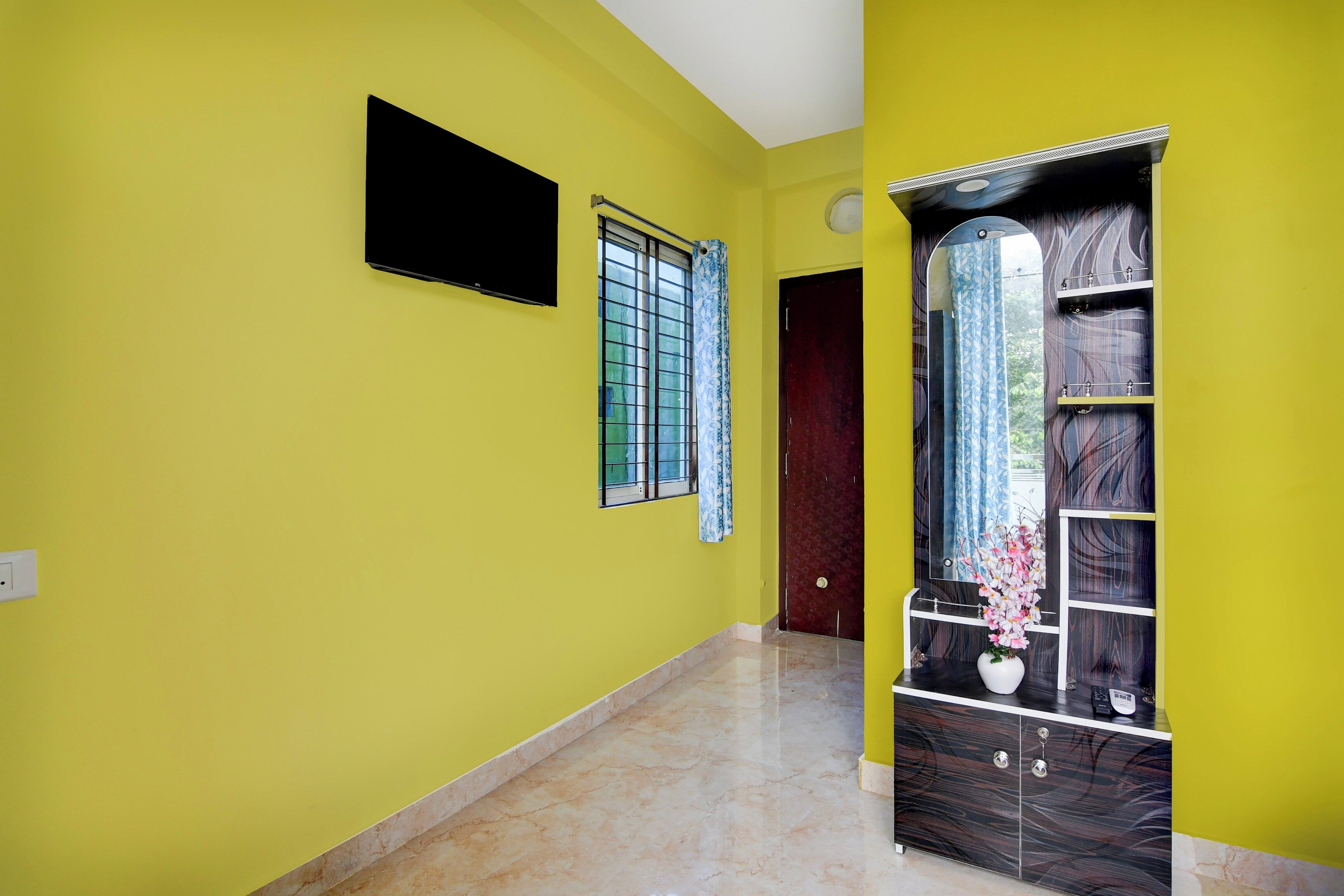 A hallway with yellow walls, a tiled floor, a door, and a mirror with a decorative vase.