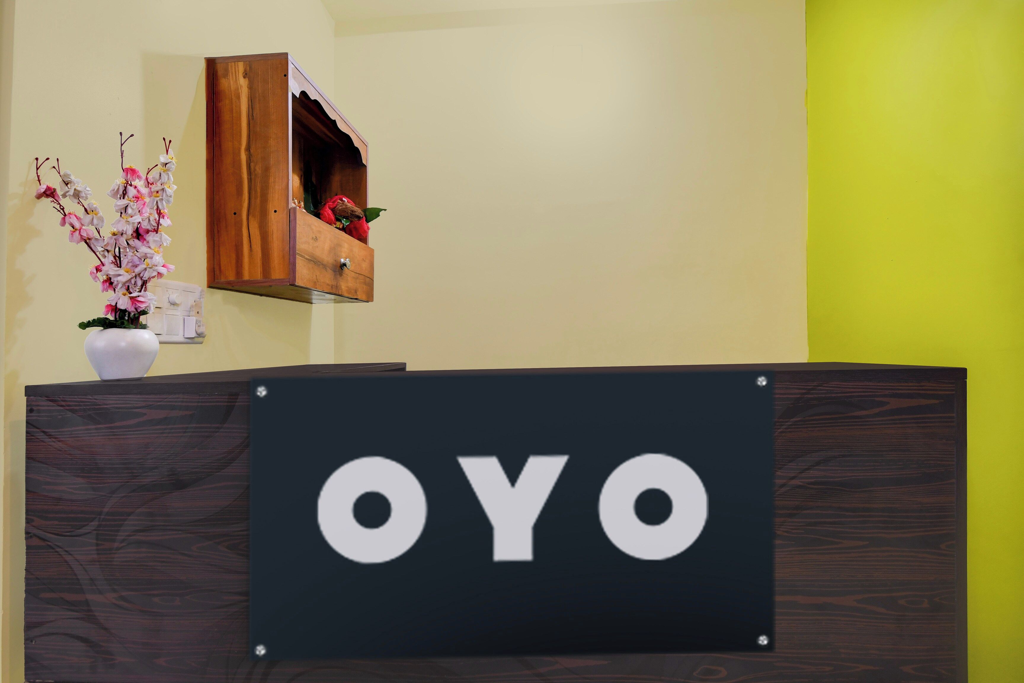 A reception desk with a sign that reads 'OYO' and a wooden shelf above it with a vase of flowers.