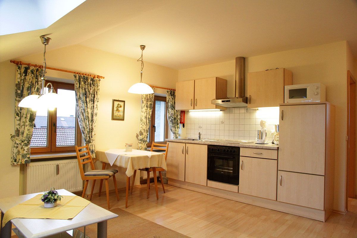 A compact kitchen with a dining area, wooden cabinets, a microwave, and a window with curtains.