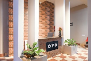 A reception area with a brick wall, a reception desk, and potted plants. - Hotel O Airport Residency (Bhubaneswar)