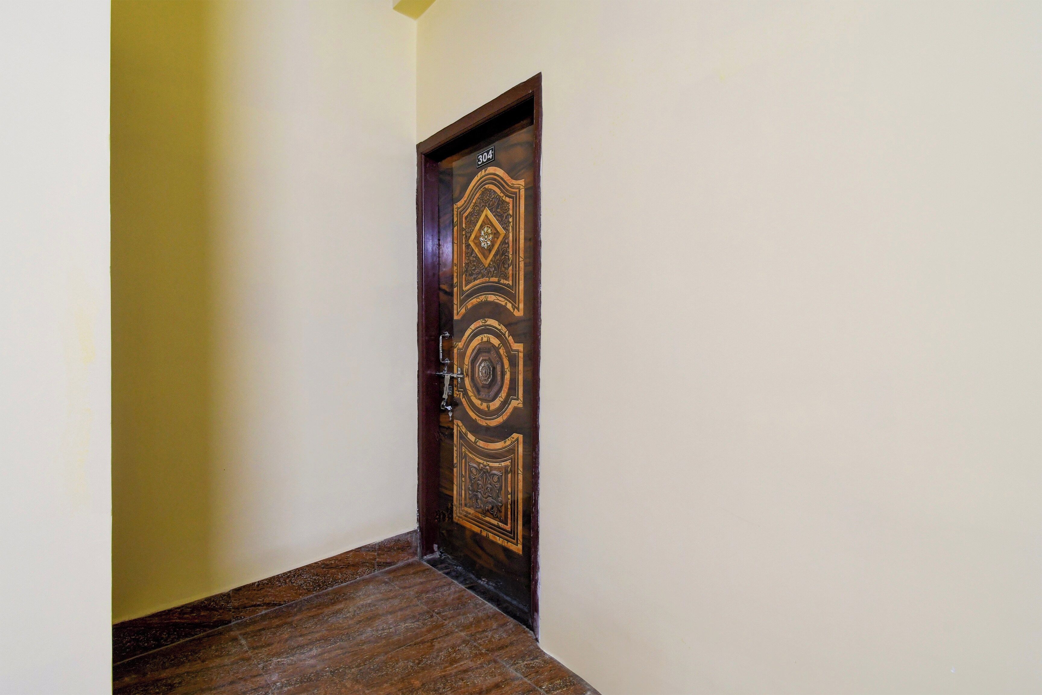 A hallway with a wooden door featuring intricate carvings and a number plate.