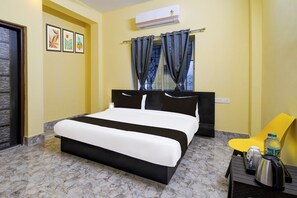 A hotel room with a bed, a chair, a table with a kettle, and a water bottle. - Hotel O Airport Residency (Bhubaneswar)
