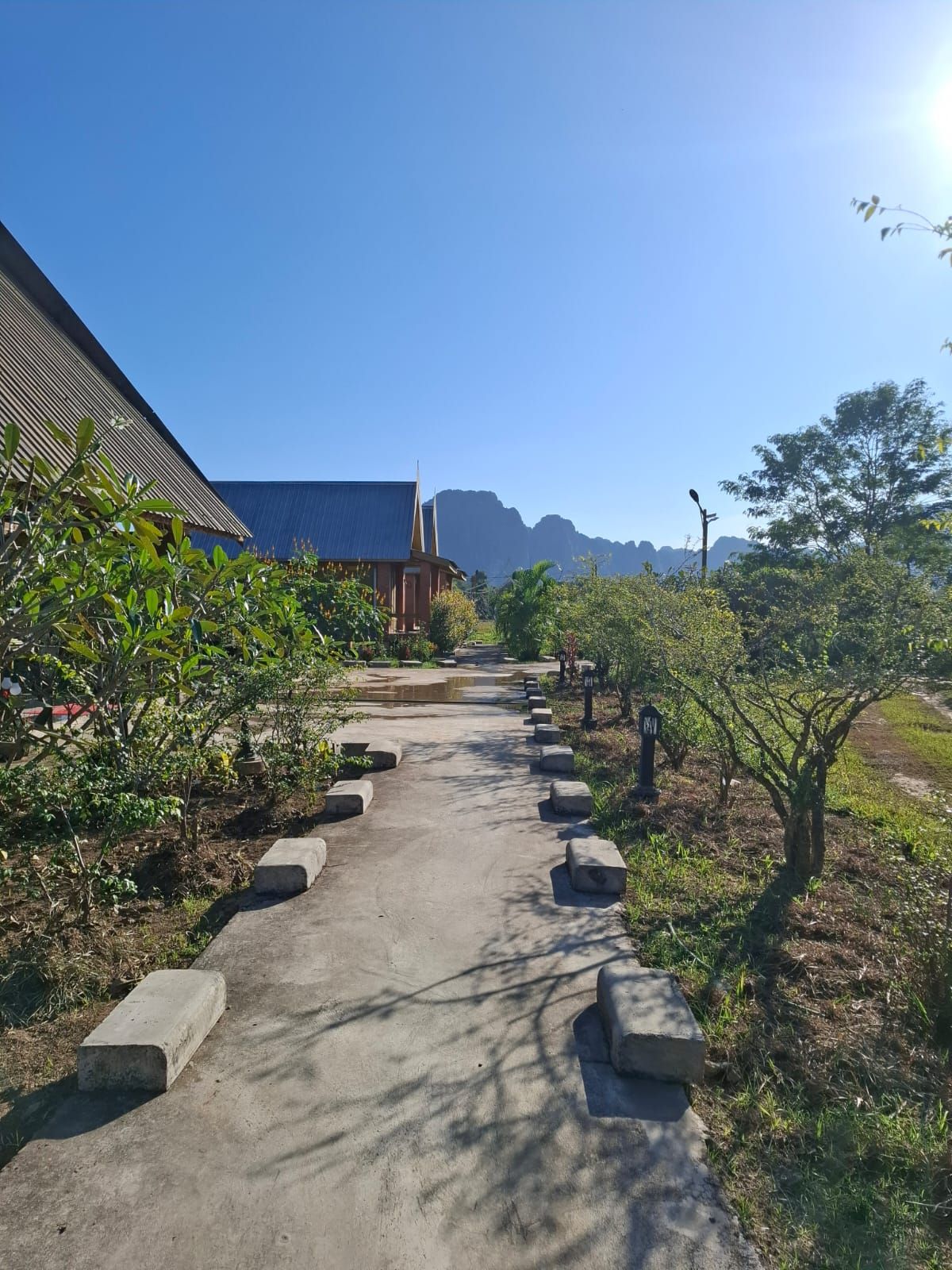 Un chemin menant à un bâtiment doté d’un toit en pente, entouré de verdure et sous un ciel dégagé.