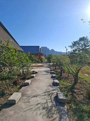 Un sendero lleva a un edificio de techo inclinado, rodeado de vegetación y un cielo despejado.