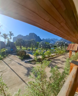 Vista desde un espacio cubierto con vistas a un complejo turístico, palmeras, sillas de descanso y montañas al fondo.