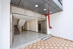 A modern interior with a staircase leading to an upper level, a fire hose on the wall, and a patterned floor. - Hotel O Vishnupriya Holiday inn (Bhubaneswar)
