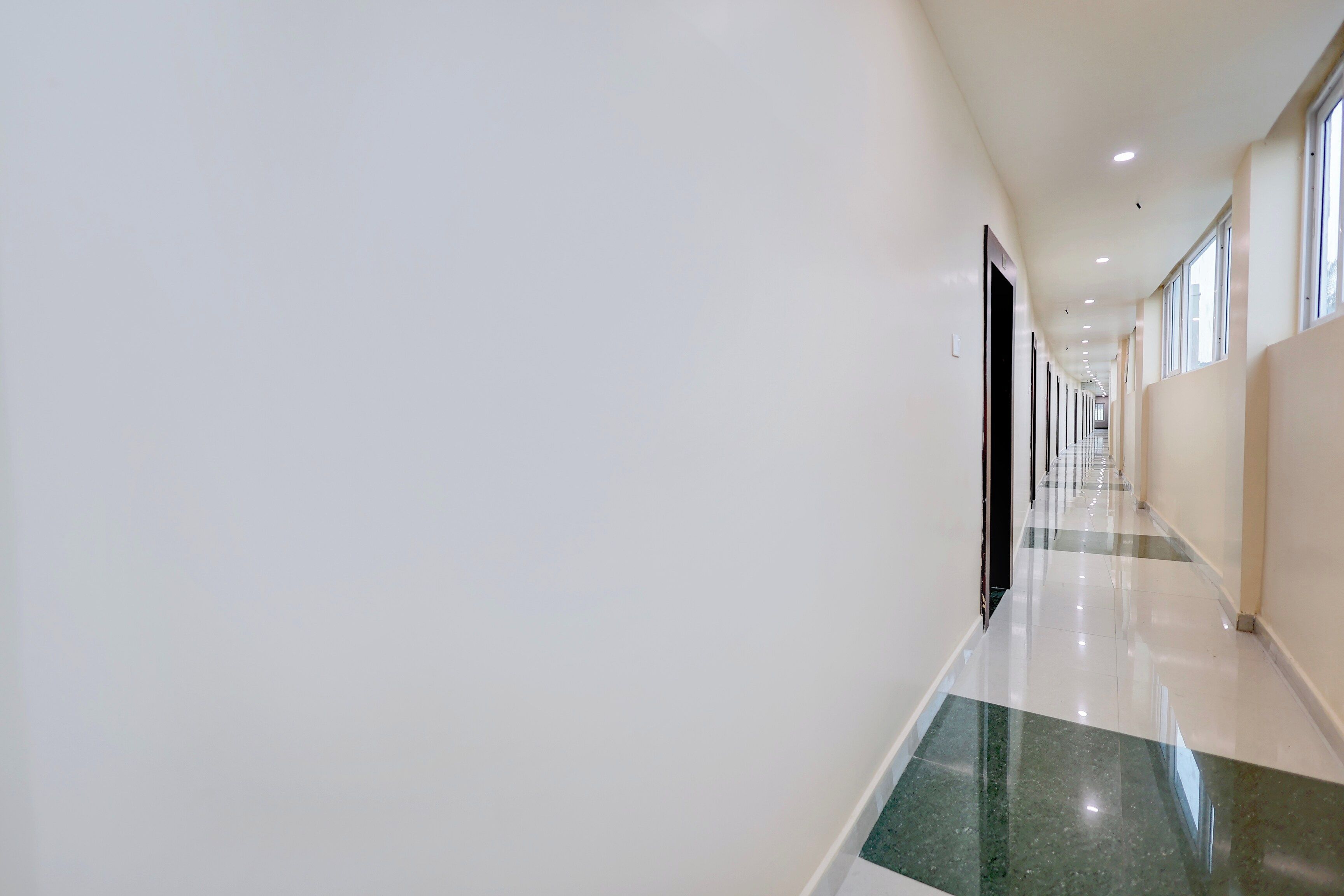 A long, straight hallway with a shiny floor, white walls, and doors on one side.