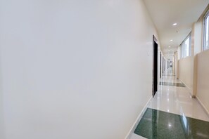A long, straight hallway with a shiny floor, white walls, and doors on one side. - Hotel O Vishnupriya Holiday inn (Bhubaneswar)
