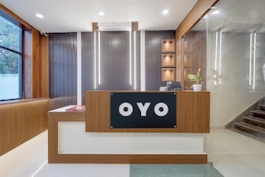 A reception desk with a sign that reads 'OYO' in a modern hotel lobby with wooden paneling and a staircase. - Hotel O Vishnupriya Holiday inn (Bhubaneswar)