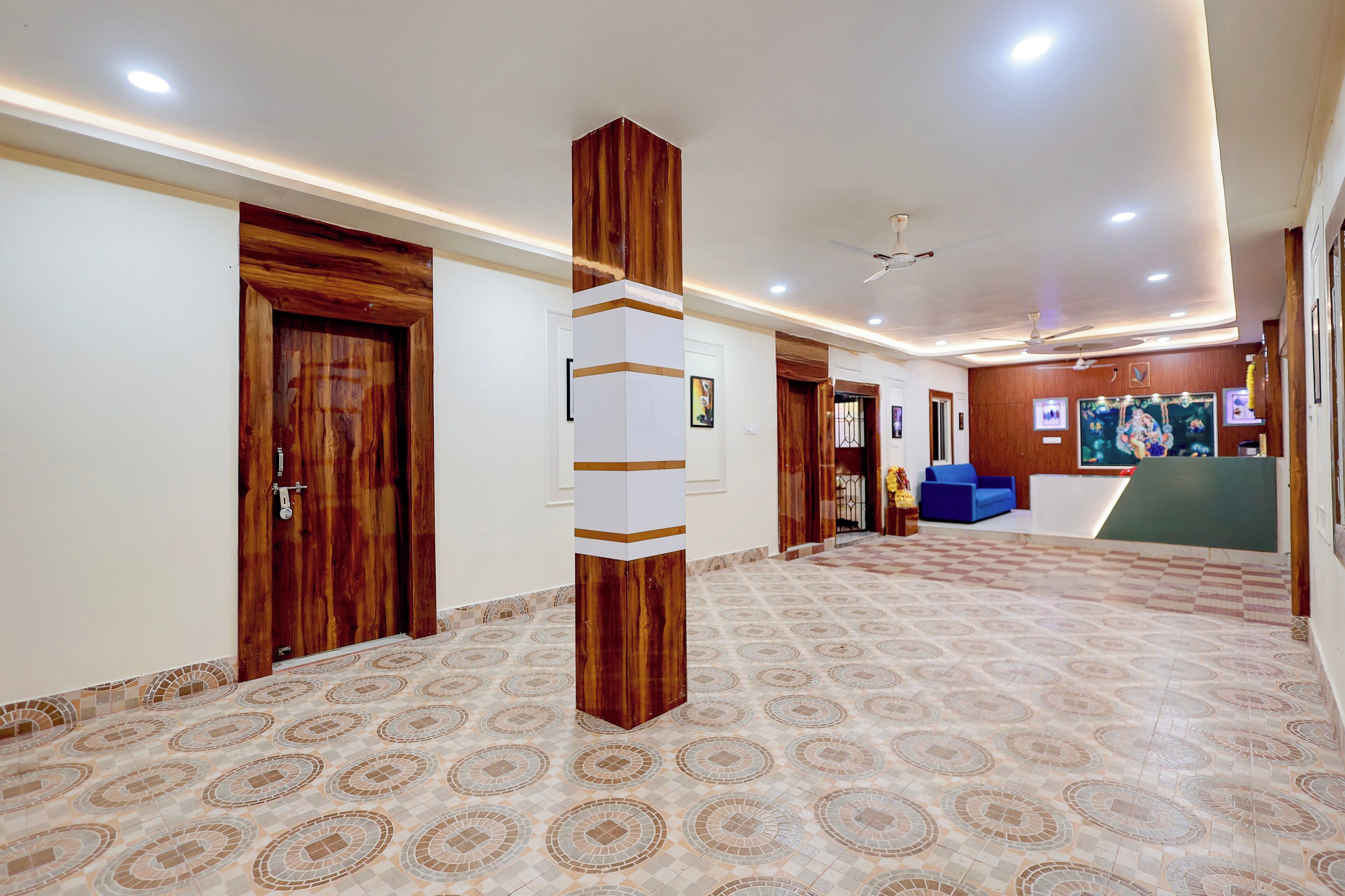 A hotel lobby with a patterned floor, wooden doors, a reception desk, and a ceiling fan.