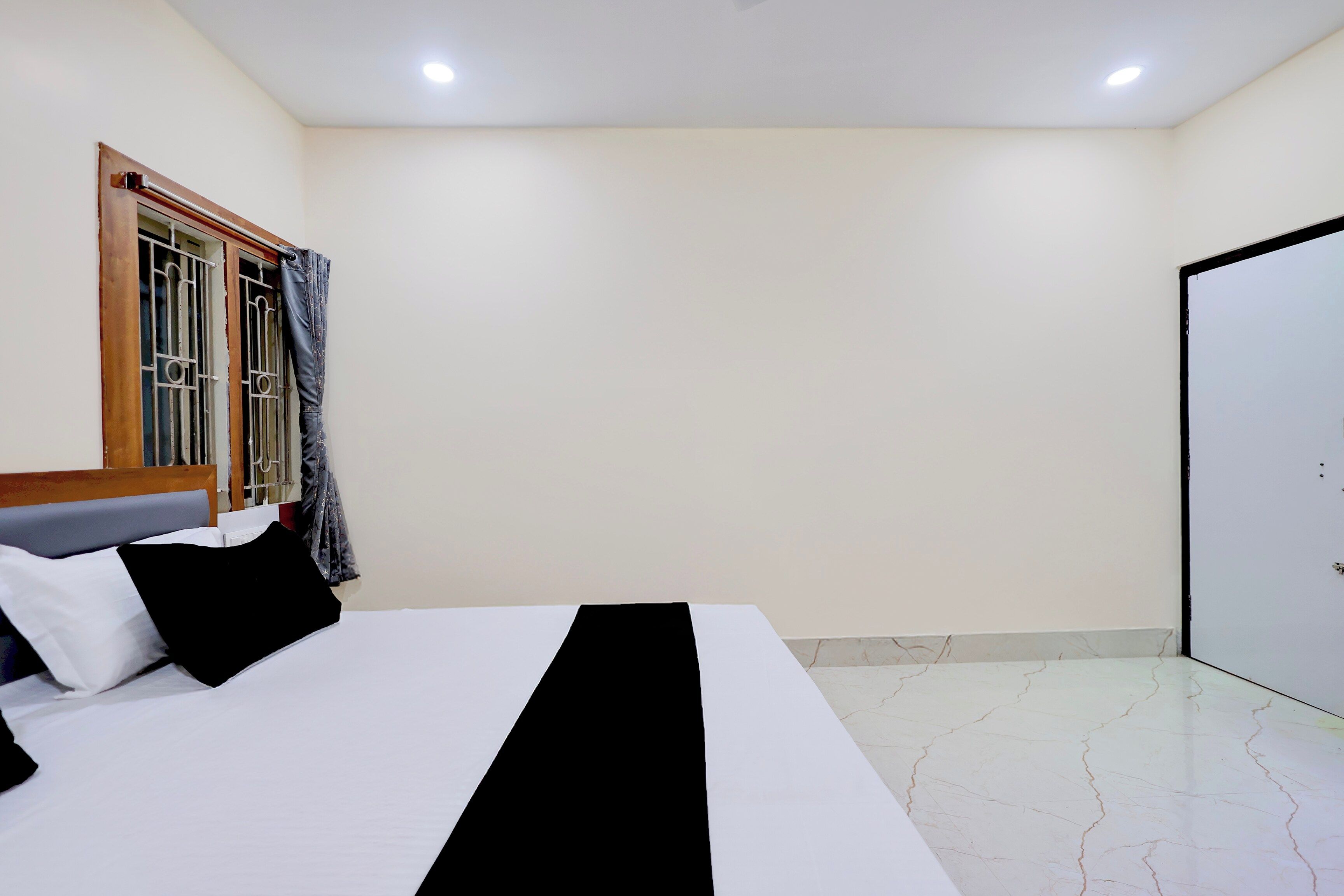 Un dormitorio con una cama, una ventana con barrotes, una puerta y piso de baldosas.