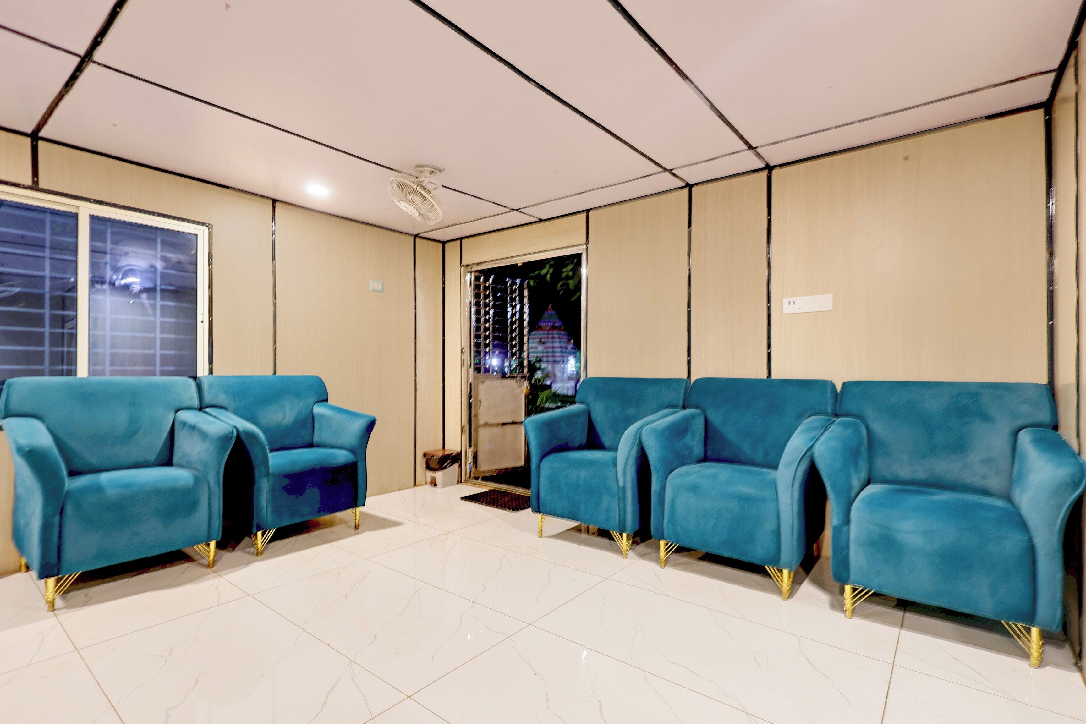 A waiting area with four blue chairs, a tiled floor, a ceiling fan, and a door leading outside.