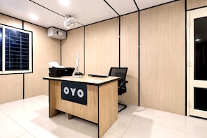 A conference room with a wooden desk labeled 'OYO,' a projector, a black office chair, and a window with blinds. - Hotel O Sky Plex Guest House (Bhubaneswar)