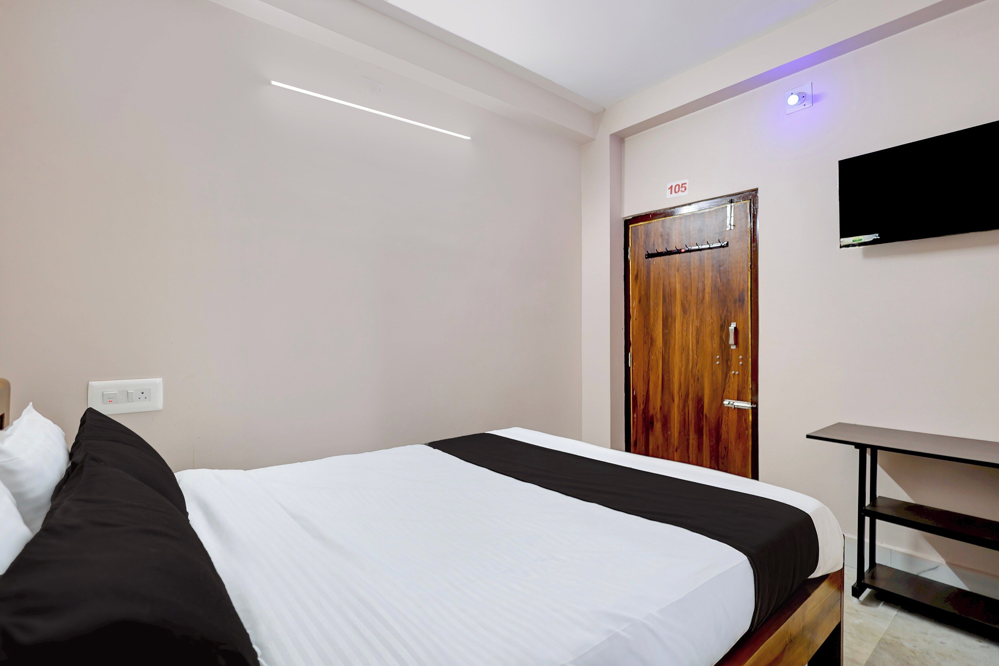 A hotel room with a bed, a wooden door, a flat-screen TV mounted on the wall, and a small table.