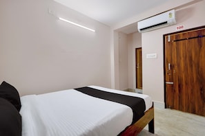 A bedroom with a bed, an air conditioner, a wooden door, and a light switch. - Hotel O Temple City Guest House (Bhubaneswar)