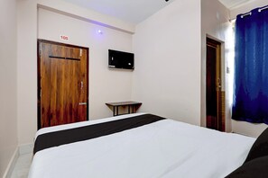 A hotel room with a bed, a small table, a TV mounted on the wall, and a door with a number sign. - Hotel O Temple City Guest House (Bhubaneswar)
