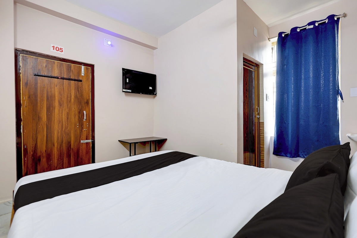 A hotel room with a bed, a small table, a TV mounted on the wall, and a door labeled '105'.