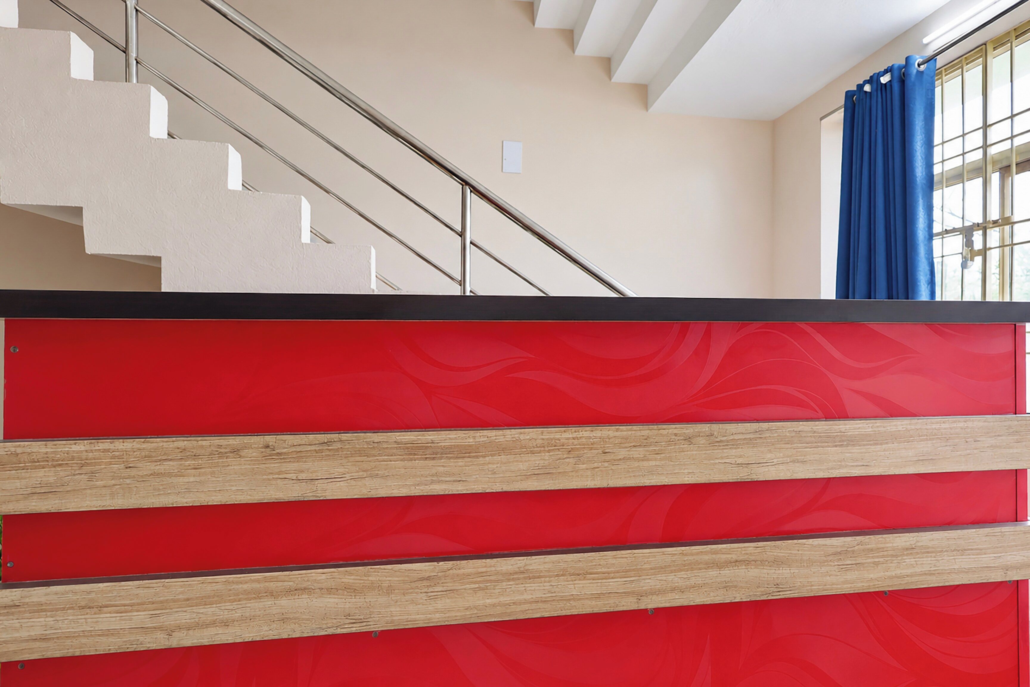 A staircase with a beige wall and a red panel at the bottom.