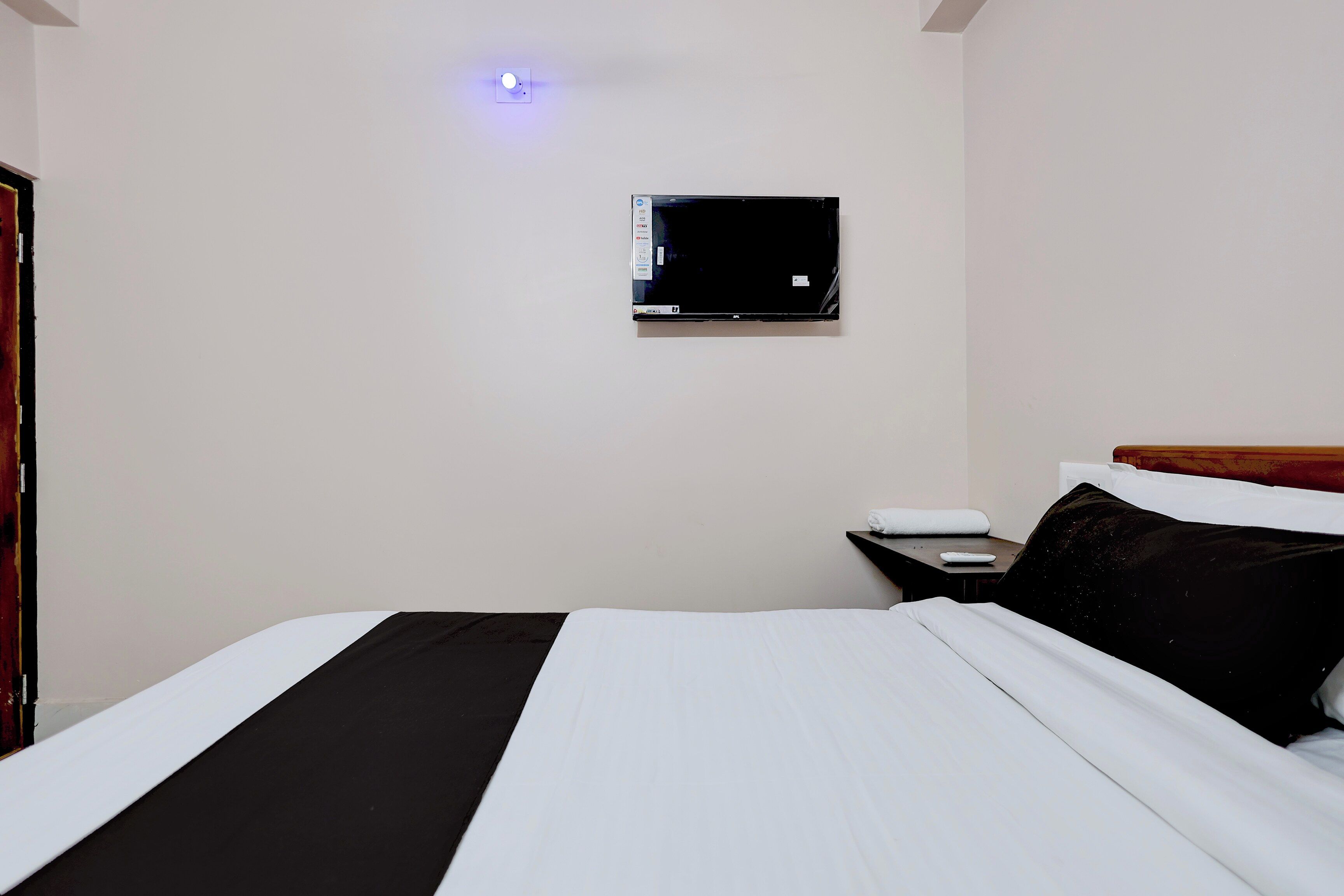A hotel room with a bed, a bedside table, a flat-screen TV mounted on the wall, and a door.