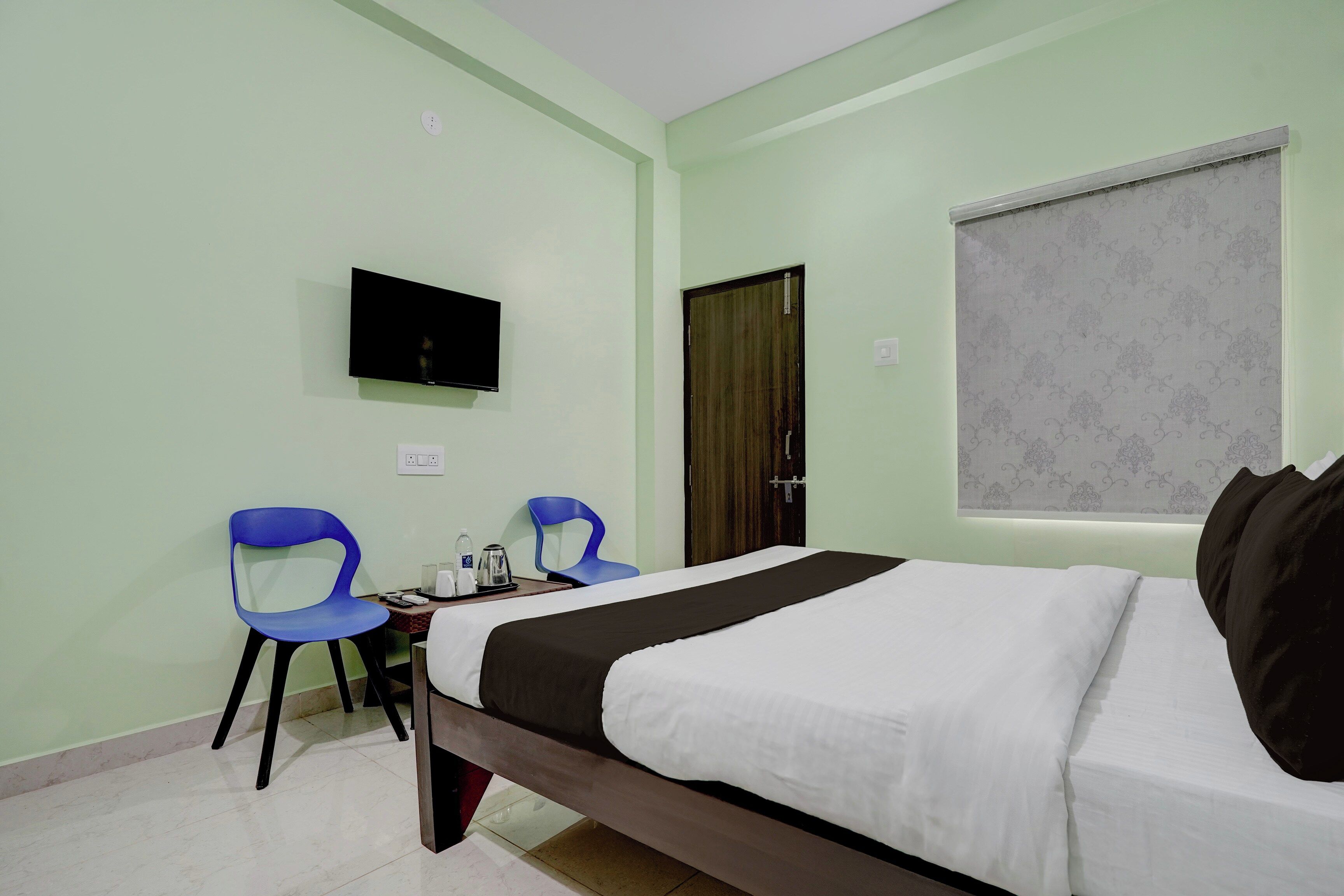 Habitación de hotel con cama, dos sillas, televisor y ventana con cortina.