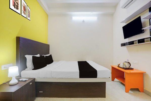 Una habitación de hotel con cama, mesita de noche, lámpara y televisor montado en la pared.