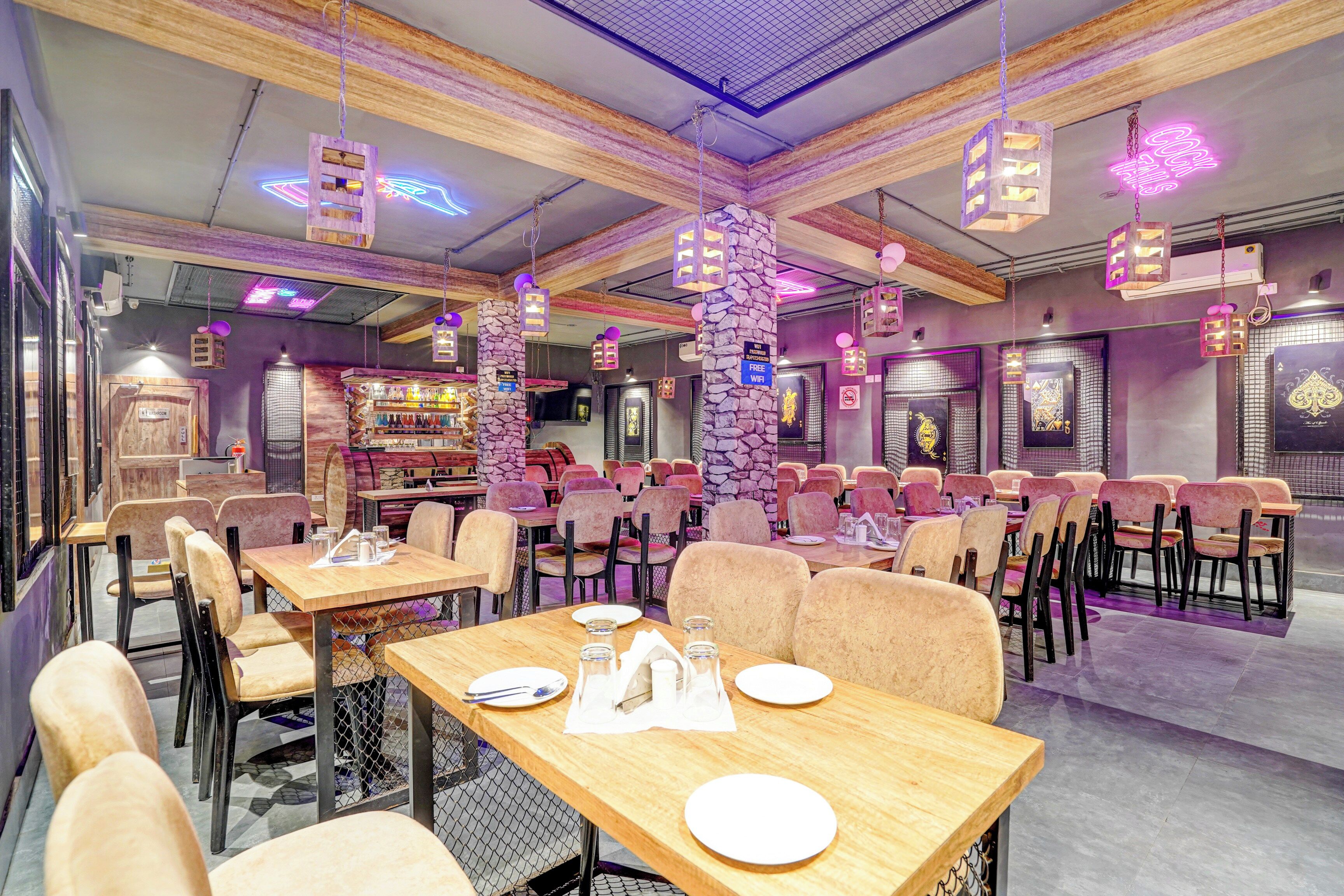 A restaurant interior with multiple tables and chairs, neon signs, and a stone pillar.