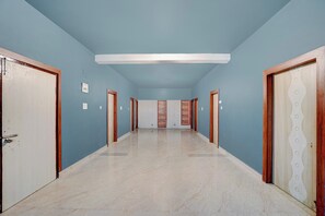 Un couloir avec un mur bleu clair, des portes en bois et un sol en marbre.