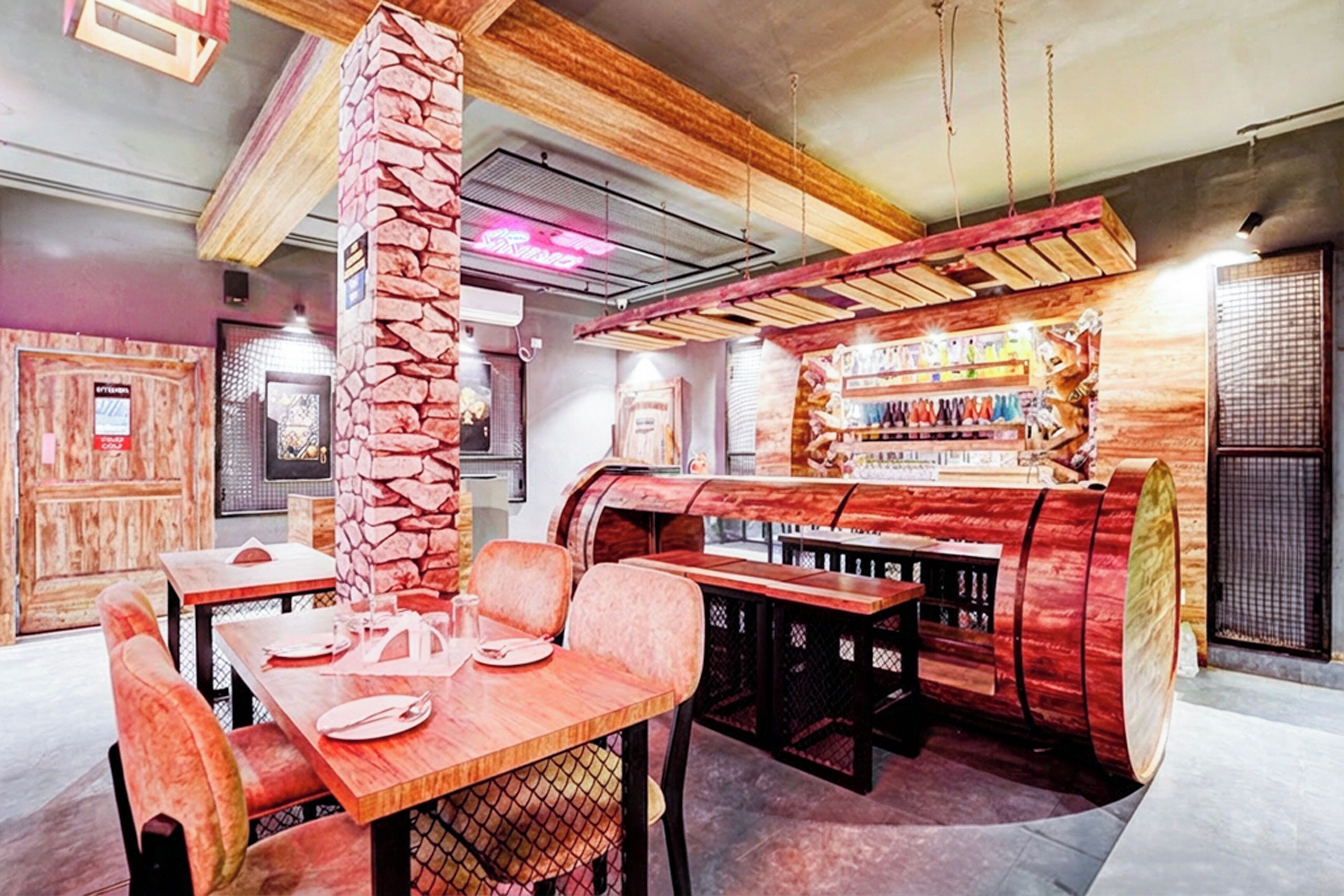 Interior de restaurante con mesas de madera, pilares de piedra y una zona de bar con botellas.