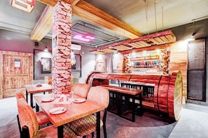 L’intérieur d’un restaurant avec des tables en bois, des piliers en pierre et un bar où sont exposées des bouteilles.