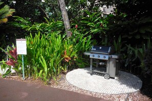 A barbecue grill with a sign, surrounded by lush greenery and a paved area. - On the beach sleeps 6 with 2 bedrooms 4 star quality resort sunsets & amenities (Kihei)