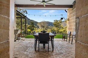 Eine Außenpatio mit Tisch und Stühlen, einem Deckenventilator, Lichterketten und Blick auf eine Berglandschaft.