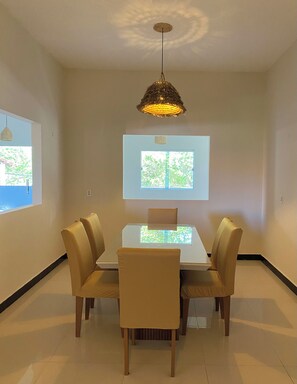 Un espace repas comprenant une table, des chaises, un luminaire au plafond et une fenêtre.