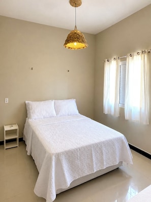 Una camera da letto con un letto, un comodino, una lampada a sospensione e una finestra con tende.