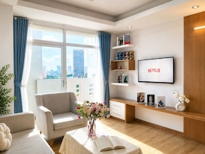 A modern living room with a sofa, a coffee table with a book and flowers, a TV on the wall, and a city view. - Spacious 2BR Apt near Ben Thanh Market & D1 Free Wifi (Thành phố Hồ Chí Minh)