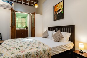 Un dormitorio con cama, almohadas, una mesita de noche, una lámpara, un cuadro y una puerta que da a un balcón.