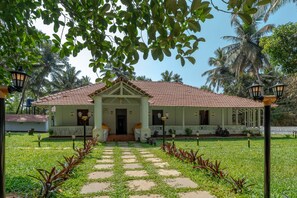Un bâtiment de style colonial à deux étages, doté d’un toit en tuiles, d’une entrée centrale et d’un chemin de jardin menant à l’entrée.