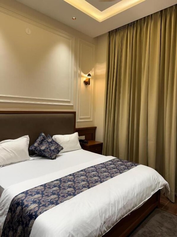 A hotel room with a large bed, a headboard, a nightstand, and a window with curtains.