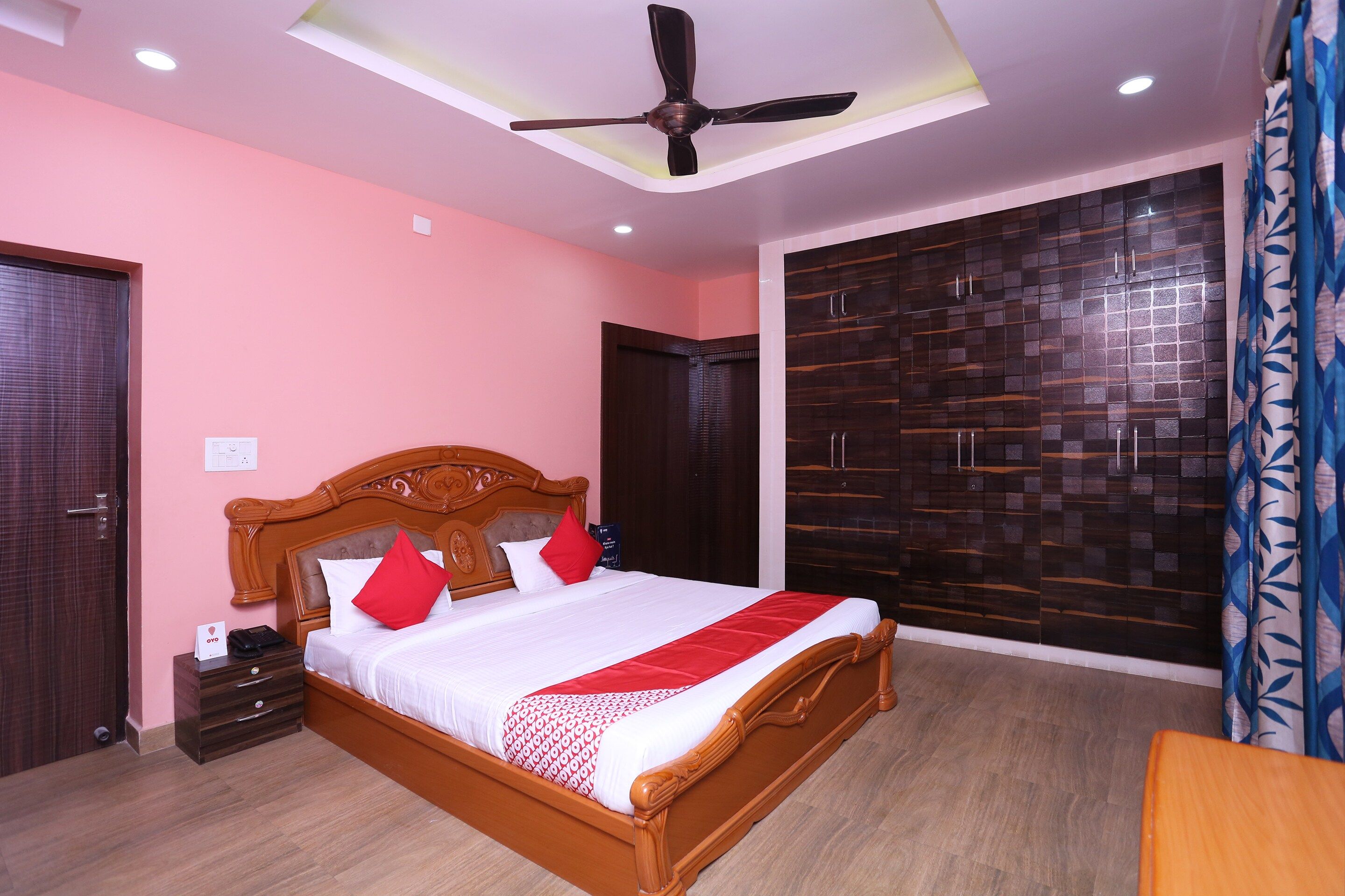 Un dormitorio con cama de madera, ventilador de techo, armario grande y cortina estampada.