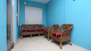 A room with two wicker sofas with red cushions, a white curtain, and a tiled floor.